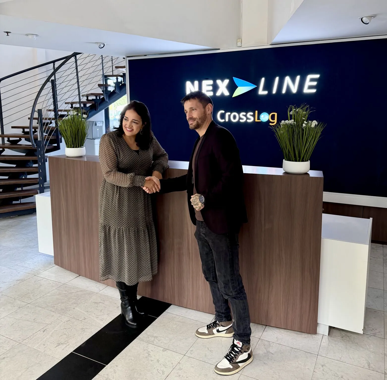 Deux représentants du partenariat Nexline et US Lesquin échangent une poignée de main dans les locaux de Nexline, devant le logo de l'entreprise.